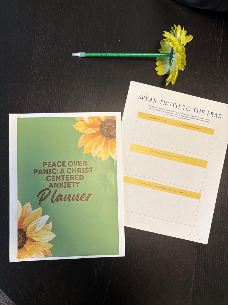 May include: A planner titled "Peace Over Panic: A Christ-Centered Anxiety Planner" with a green cover and sunflower illustrations. A pen with a yellow flower is on top of the planner and a worksheet that says "Speak Truth to the Fear".