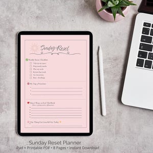 May include: A pink digital planner with the text "Sunday Reset" in a black script font. The planner includes a weekly reset checklist, top priorities, how I want to feel this week, and one thing I'm grateful for today. The planner is displayed on a tablet with a white stylus next to it.
