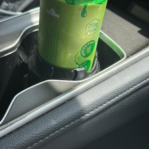 May include: A bright green aluminum beverage can with a silver top sits inside a black plastic cup holder. The can features text that reads 200mg CAFFEINE and GLUTEN-FREE, along with a graphic of a lime slice on the lower portion of the can.