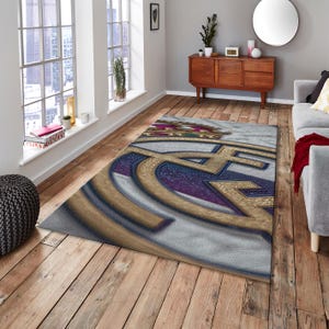 May include: A rectangular area rug featuring a large, centered emblem with a gold crown at the top. The design incorporates a prominent gold letter C intertwined with a gold letter F, set against a textured background of deep purple and white.