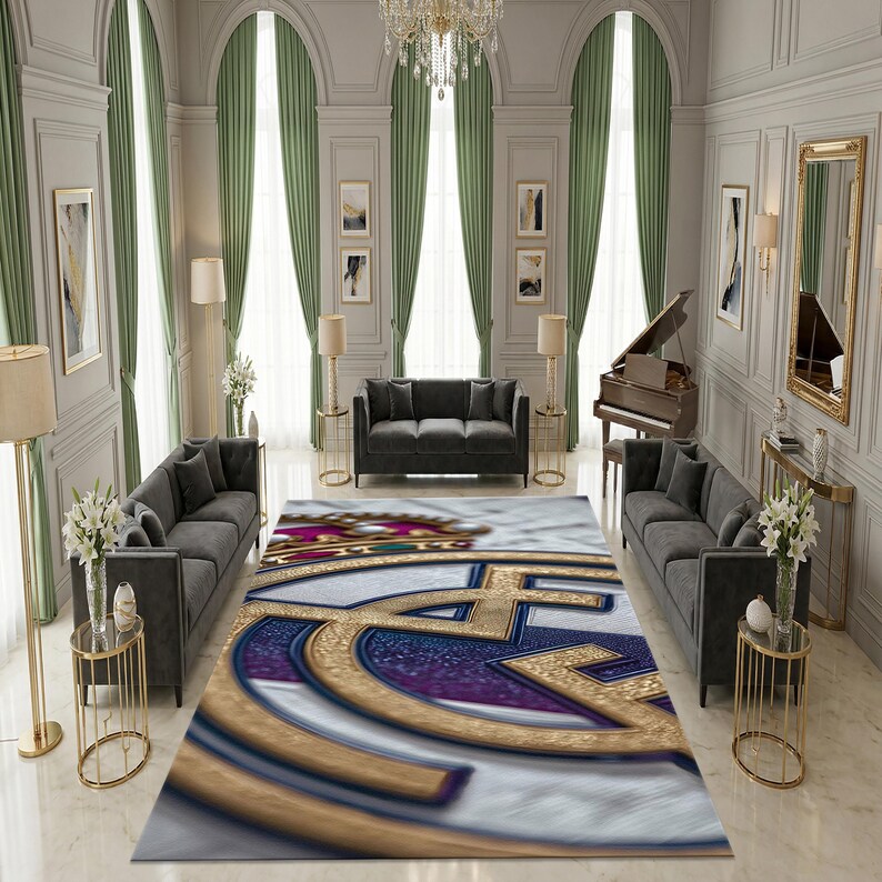 May include: A rectangular area rug featuring a large, centered gold and blue emblem with a crown motif at the top. The design is set against a white background with a textured, marble-like appearance, filling the floor space between two gray sofas.