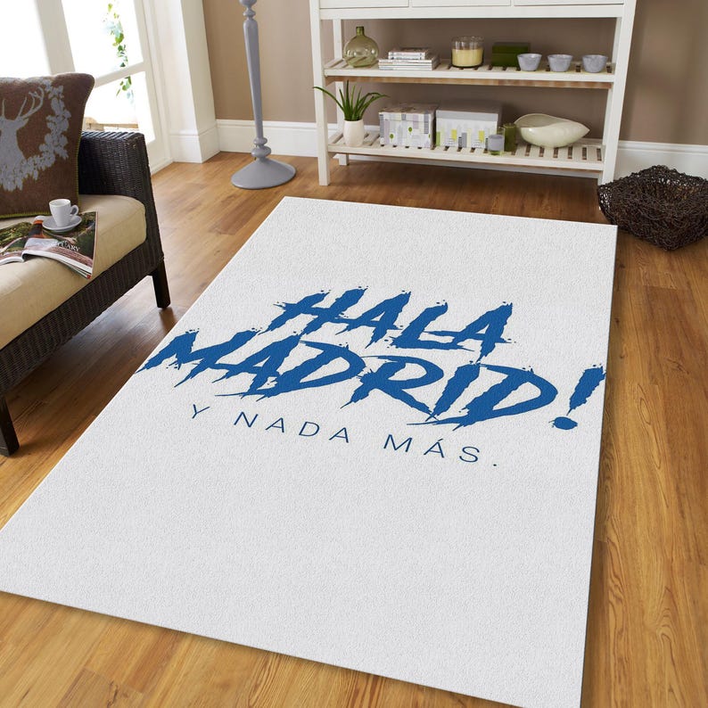 May include: White rectangular rug with the words "HALA MADRID!" in blue brushstroke font. Below the text is "Y NADA M&Aacute;S." The rug is on a hardwood floor.