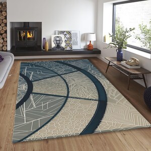 Puede incluir: Una alfombra con estampado geométrico en tonos azul marino, gris y beige. La alfombra presenta un círculo grande con un diseño geométrico blanco y un círculo más pequeño con un patrón de puntos blancos.