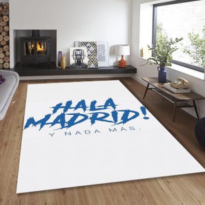 May include: White rectangular rug with the words "HALA MADRID!" in blue, and "Y NADA M&Aacute;S." below. The rug is in a room with a fireplace, artwork, and a wooden table.