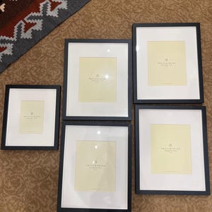May include: Five black picture frames with white mats and a cream-colored background. Each frame has the text "Pottery Barn" printed in black at the bottom.