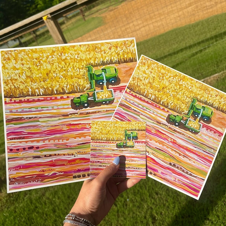 May include: Three square art prints featuring a painted scene of a green combine harvester working in a golden cornfield. The foreground displays horizontal bands of pink, red, orange, and white paint strokes, creating a textured, abstract landscape.