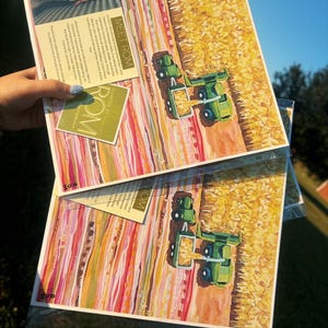 May include: Two identical art prints in clear plastic sleeves featuring a green tractor harvesting a yellow cornfield. The artwork includes horizontal bands of pink, orange, and red colors. A small card with the text "MEET ROM" is attached to the top.