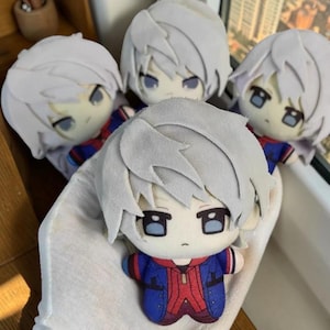May include: Four plush dolls featuring white hair, large dark eyes, and a serious expression. Each doll wears a blue and red jacket with a central red panel. The dolls have a soft, fabric texture and are arranged in a group, with one doll held in the foreground.
