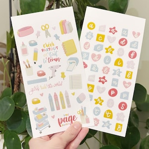 Peut inclure: Deux planches d'autocollants blancs avec des illustrations colorées et du texte. L'une présente des articles de papeterie comme des ciseaux, des crayons et un pistolet à colle, avec le texte "créer partout et tout le temps" et "girls rule the world". L'autre a des lettres et des formes de l'alphabet.