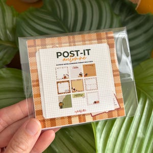 Peut inclure: Un paquet de notes adhésives carrées avec des illustrations sur le thème de l'automne et des motifs quadrillés. L'emballage affiche le texte POST-IT automne et 10 STICKY NOTES ADHESIVES FORMAT 8CM X 8CM. Les notes sont sous film plastique.