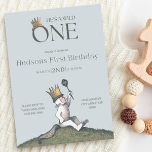 Puede incluir: Una tarjeta de invitación azul y blanca con una ilustración de dibujos animados de un personaje salvaje del libro Donde viven los monstruos. El texto de la tarjeta dice "He's a Wild One" y "Hudson's First Birthday" con la fecha y la hora de la fiesta.
