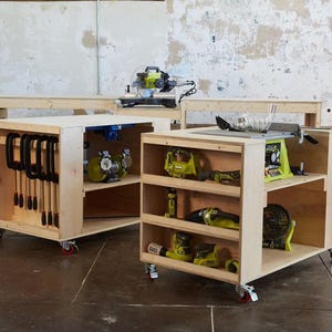 Może przedstawiać: Drewniane jednostki do przechowywania w warsztacie na kółkach. Jednostki wykonane są z jasnego drewna i posiadają otwarte półki i schowki na narzędzia. Widoczne są różne elektronarzędzia, w tym piła tarczowa i piła stołowa. Jednostki znajdują się w warsztacie.
