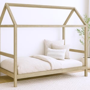 以下が含まれることがあります： マットレス、枕、羽毛布団を備えた、明るい色の木製ハウスベッドフレーム。 ベッドフレームは家型です。 部屋はサイドテーブル、植物、柄のラグで装飾されています。 ベッドフレームの長さは約190cmです。