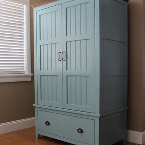May include: A tall, light blue wooden cabinet with a dark brown top and a drawer at the bottom. The cabinet has two doors with vertical paneling and black handles. The cabinet is approximately 72 inches tall.
