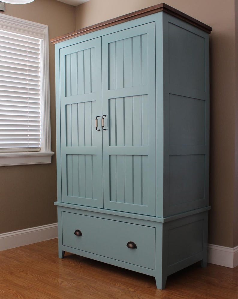May include: A tall, light blue wooden cabinet with a dark brown top and a drawer at the bottom. The cabinet has two doors with vertical paneling and black handles. The cabinet is approximately 72 inches tall.