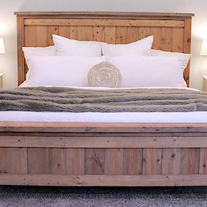 May include: A rustic wooden bed frame with a matching headboard. The bed is made of light brown wood and has a simple, clean design. White pillows and a gray blanket adorn the bed. Two white nightstands with lamps flank the bed.
