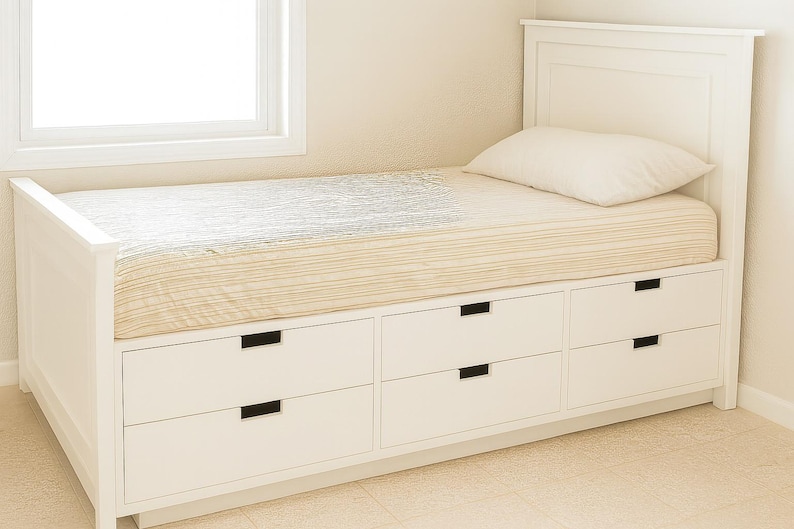 May include: A white twin-sized bed with a headboard and six storage drawers. The bed has a beige and white striped mattress and a white pillow. The bed is placed near a window.