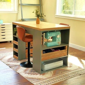 May include: A sewing room setup featuring a teal sewing machine on a gray and wood table. The table has a wooden top and storage shelves. An orange chair is positioned at the table. A wooden crate and a printer are stored on the shelves.