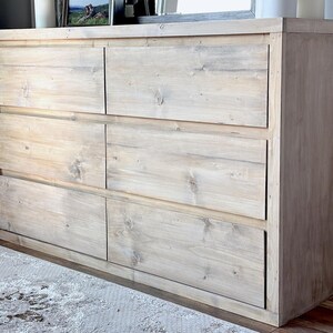 May include: A light-colored wooden dresser with six drawers. The dresser is made of light-colored wood and has a simple, modern design. The drawers are arranged in two columns of three.