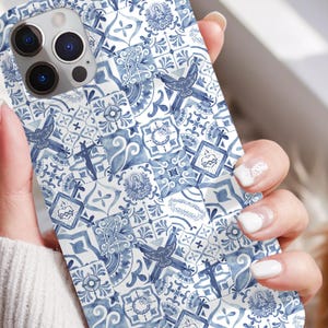 May include: A white and blue patterned phone case with a decorative tile design is held in a person's hand. The case features a repeating pattern of blue floral and geometric shapes. The text "Pax Sanctorum" is visible at the bottom of the image.