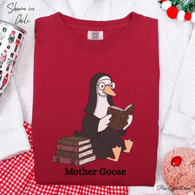 K&ouml;nnte beinhalten: Ein rotes Sweatshirt mit einer Grafik einer Gans, die als Nonne gekleidet ist, eine Brille tr&auml;gt und ein Buch liest. Der Text "Mother Goose" ist darunter gedruckt. Das Sweatshirt hat einen Rundhalsausschnitt und lange &Auml;rmel.