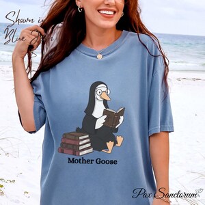 K&ouml;nnte beinhalten: Hellblaues T-Shirt mit einer Cartoon-Gans in Nonnenkluft, die ein Buch liest. Unter der Illustration steht der Text "Mother Goose". Das Shirt tr&auml;gt auch die Aufschrift "Shown in Blue" und "Pax Sanctorum".