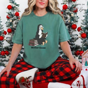 K&ouml;nnte beinhalten: Ein gr&uuml;nes T-Shirt mit einer Cartoon-Gans in Nonnentracht, die ein Buch liest, mit dem Text "Mother Goose" darunter. Die Gans sitzt auf B&uuml;chern. Die Person tr&auml;gt eine rot-schwarz karierte Pyjamahose.