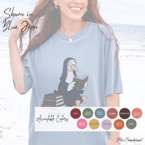 K&ouml;nnte beinhalten: Hellblaues T-Shirt mit einer Cartoon-Illustration eines Pinguins, der eine Brille tr&auml;gt und ein Buch liest. Der Text "Shown in Blue Jean" steht oben links. Unten sind verf&uuml;gbare Farben aufgelistet.