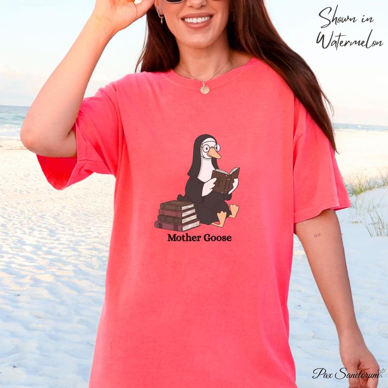 K&ouml;nnte beinhalten: Ein korallenfarbenes T-Shirt mit einer Cartoon-Gans in Nonnentracht, die ein Buch liest, mit dem Text "Mother Goose" darunter. Das Shirt ist mit "Shown in Watermelon" beschriftet und hat unten ein kleines Logo.