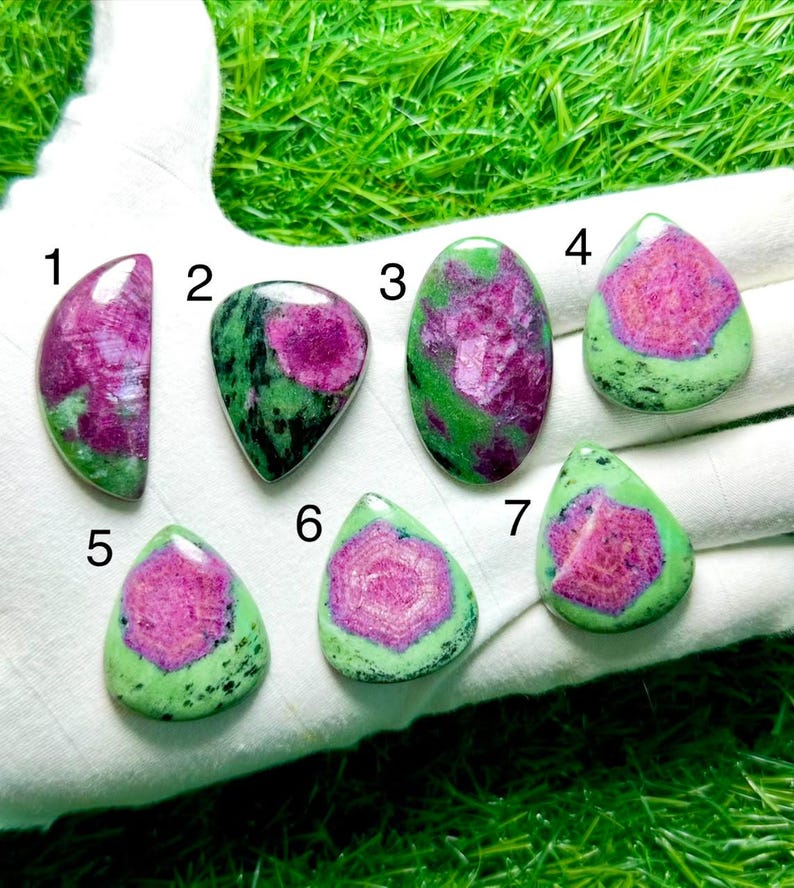 Pu&ograve; includere: Sette pietre preziose levigate di rubino in zoisite numerate da 1 a 7. Ogni pietra presenta un centro magenta o rosa vibrante circondato da inclusioni minerali verdi e nere maculate. Le forme variano tra goccia, ovale e semicerchio.