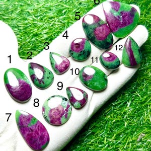 Può includere: Una collezione di dodici cabochon in rubino zoisite lucidati, ognuno caratterizzato da una distinta miscela di vivaci inclusioni di rubino magenta-rosa all'interno di una matrice di zoisite verde. Le pietre sono numerate da uno a dodici e hanno forme varie.