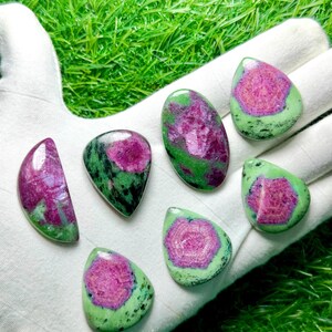Pu&ograve; includere: Sette cabochon levigati di zoisite con inclusioni di rubino, caratterizzati da vivaci centri magenta circondati da pietra verde e nera maculata. Le pietre sono modellate in varie forme a goccia, ovali e semicircolari con superfici lisce e lucide.