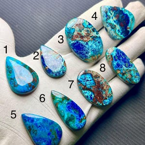 May include: Eight polished, teardrop and oval-shaped gemstones featuring vibrant blue, turquoise, and brown marbled patterns. Each stone is numbered from one to eight, displaying unique color variations and smooth, reflective surfaces.