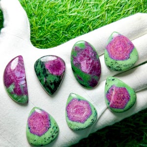 Pu&ograve; includere: Sette cabochon levigati di rubino in zoisite di varie forme, tra cui a goccia, ovale e a mezzaluna. Ogni pietra presenta un centro magenta-rosa vibrante circondato da una matrice minerale verde e nera maculata con una finitura liscia.