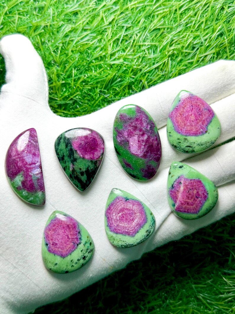 Pu&ograve; includere: Sette cabochon levigati di rubino in zoisite di varie forme, tra cui a goccia, ovale e a mezzaluna. Ogni pietra presenta un centro magenta-rosa vibrante circondato da una matrice minerale verde e nera maculata con una finitura liscia.