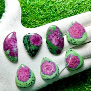 Pu&ograve; includere: Sette cabochon levigati di rubino in zoisite, ognuno con un vivace centro magenta-rosa circondato da inclusioni minerali verdi e nere screziate. Le pietre variano in forma, includendo gocce, ovali e forme a mezzaluna.