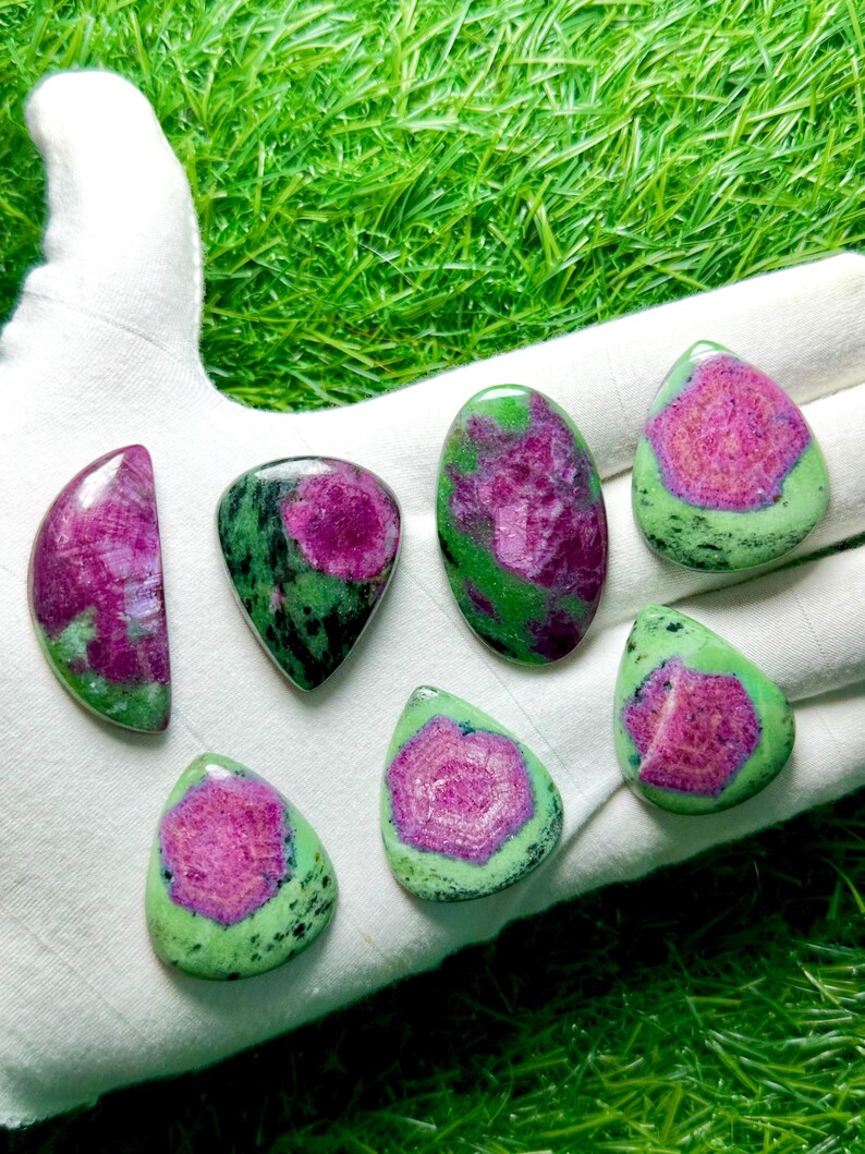 Pu&ograve; includere: Sette cabochon levigati di rubino in zoisite, ognuno con un vivace centro magenta-rosa circondato da inclusioni minerali verdi e nere screziate. Le pietre variano in forma, includendo gocce, ovali e forme a mezzaluna.