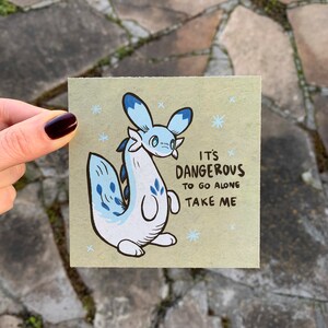 May include: A light blue and white cartoon creature with a blue fin and a light blue tail. The creature is on a beige background with the text "It's Dangerous to go alone Take me".