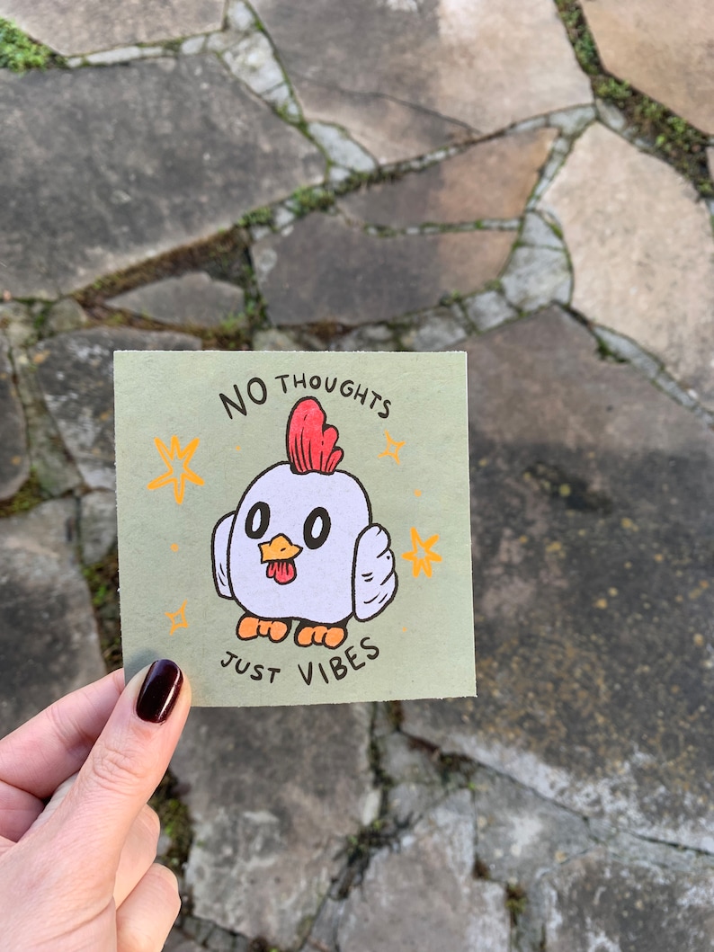 May include: A green card with a white chicken illustration and the text "NO THOUGHTS JUST VIBES". The chicken has red comb and wattles, orange feet, and black eyes. There are yellow stars around the chicken.