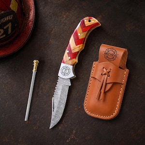 May include: A folding knife with a Damascus steel blade and a red and tan chevron-patterned handle, featuring a metal bolster engraved with a fire department emblem and the name MICHEAL. Includes a tan leather sheath and a thin metal fire starter.