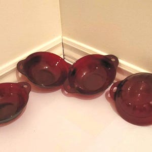 Peut inclure: Quatre bols en verre de couleur marron avec de petites poignées. Les bols de forme ovale sont posés sur une surface blanche près d'un coin. Les bols sont vides et semblent en bon état.