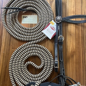May include: Equestrian equipment set featuring a black and tan rope, a black leather headstall with silver accents, and an O-ring snaffle bit. The rope is coiled, and the headstall includes a browband and a tag that reads "Always Leather".