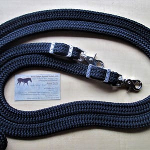 May include: A black braided horse lead rope with silver-colored hardware. The rope is coiled and lies on a light-colored surface. A small business card with a horse silhouette is also present.
