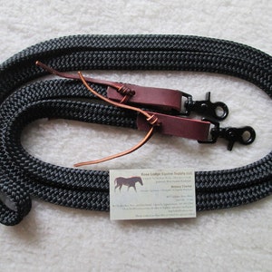May include: Black nylon rope horse reins with burgundy leather accents and black metal hardware. The reins are coiled and ready for use. A small business card is visible.