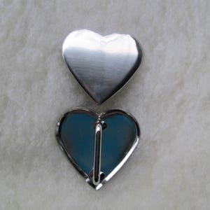 May include: A silver heart-shaped pin with a metal clasp on the back.