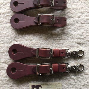 May include: Four brown leather stirrup straps with silver buckles and a silver snap hook. The straps are for use with a horse saddle.