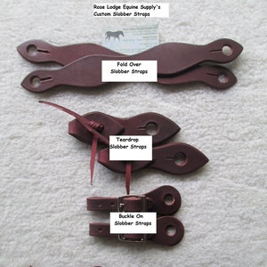 May include: Three pairs of brown leather horse slobber straps. The straps are shown in three different styles: fold over, teardrop, and buckle on. The straps are labeled with their style name.
