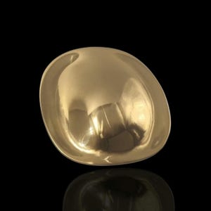 May include: A gold-colored, oval-shaped bowl with a smooth, reflective surface. The bowl's interior reflects the surrounding environment, creating a mirrored effect. The bowl is set against a black background.