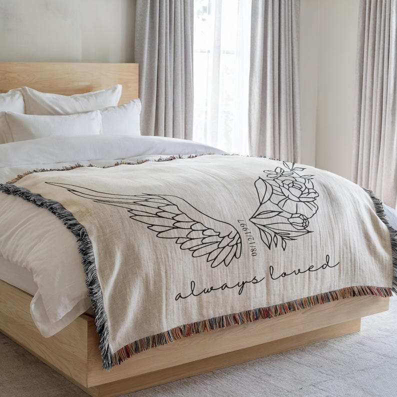 Grief gift blanket with floral angel design laid on neutral bed