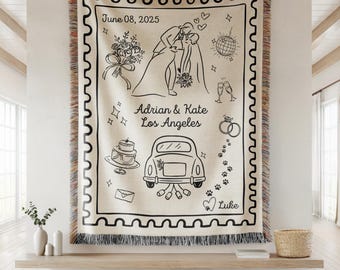 May include: Cream-colored woven throw blanket with a black line drawing of a wedding scene. The design includes a couple kissing, a cake, a car, and the text "June 08, 2025" and "Adrian & Kate Los Angeles". The blanket has a fringed edge.